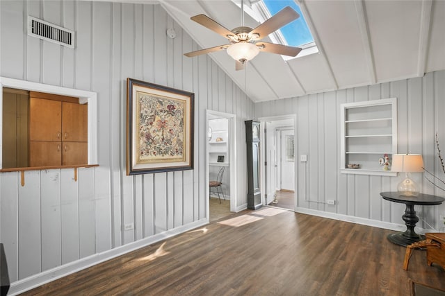 empty room with visible vents, a ceiling fan, built in features, wood finished floors, and vaulted ceiling with skylight