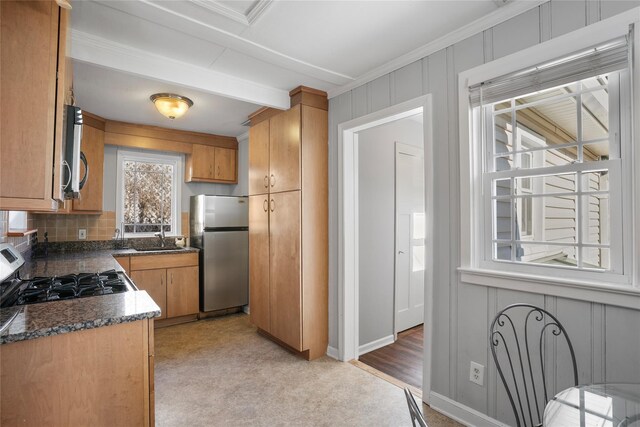 kitchen featuring brown cabinets, a sink, dark countertops, stainless steel appliances, and decorative backsplash