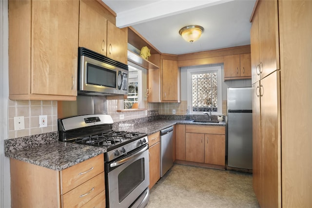 kitchen with a sink, dark stone countertops, backsplash, appliances with stainless steel finishes, and light floors