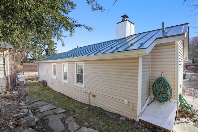 view of side of property featuring a standing seam roof, a chimney, and metal roof