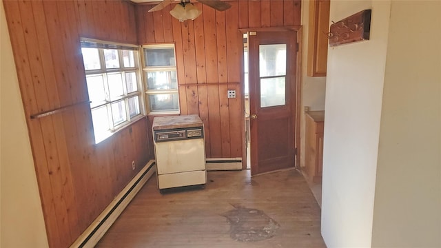 doorway to outside with wooden walls, a ceiling fan, baseboard heating, and wood finished floors