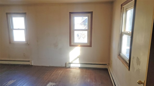 empty room with a wealth of natural light, a baseboard heating unit, and wood finished floors