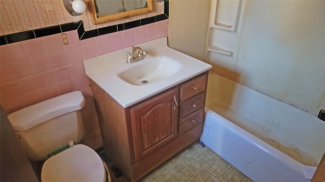 bathroom with tile walls, vanity, toilet, and wallpapered walls