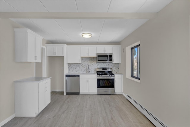 kitchen featuring white cabinets, decorative backsplash, appliances with stainless steel finishes, baseboard heating, and a sink