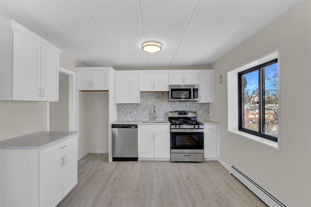 kitchen with decorative backsplash, appliances with stainless steel finishes, white cabinetry, a baseboard heating unit, and a sink