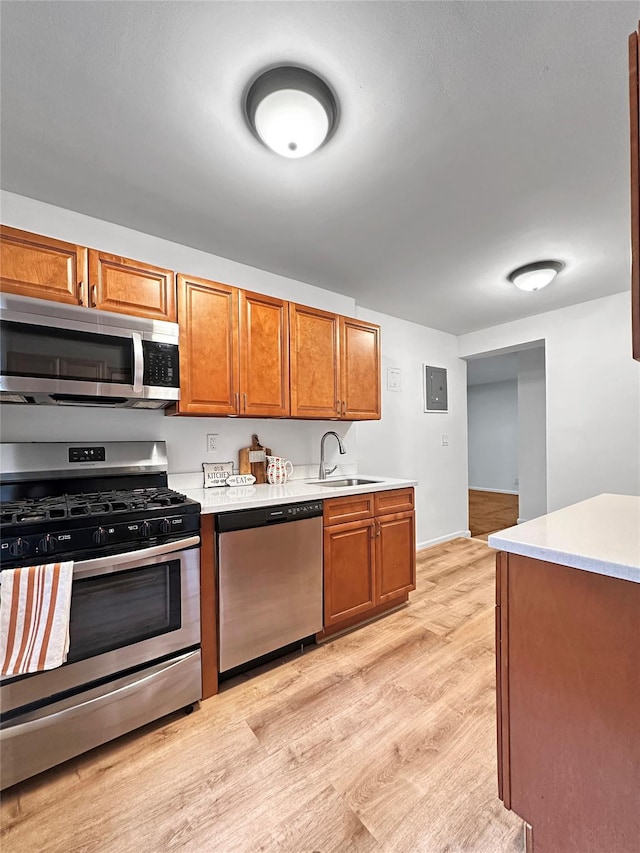 kitchen featuring light wood finished floors, light countertops, appliances with stainless steel finishes, brown cabinetry, and a sink