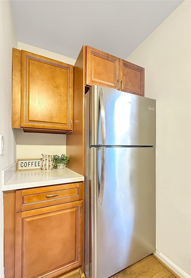 kitchen featuring baseboards, light countertops, freestanding refrigerator, brown cabinets, and light wood finished floors