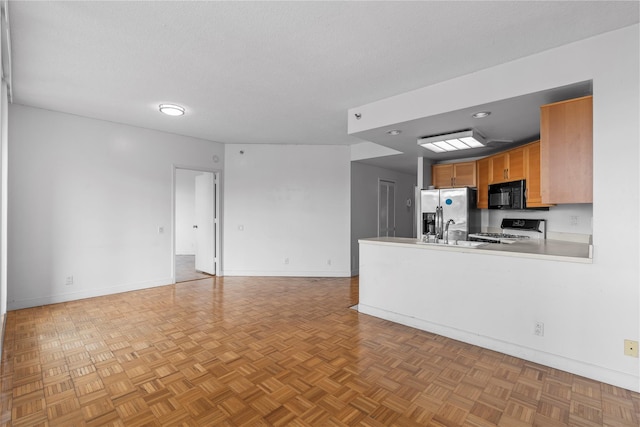 kitchen featuring black microwave, a textured ceiling, stove, open floor plan, and stainless steel fridge