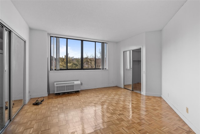 unfurnished bedroom with a wall unit AC, baseboards, and a textured ceiling