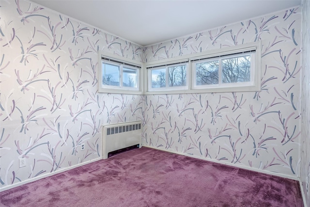 spare room featuring wallpapered walls, radiator heating unit, baseboards, and dark colored carpet