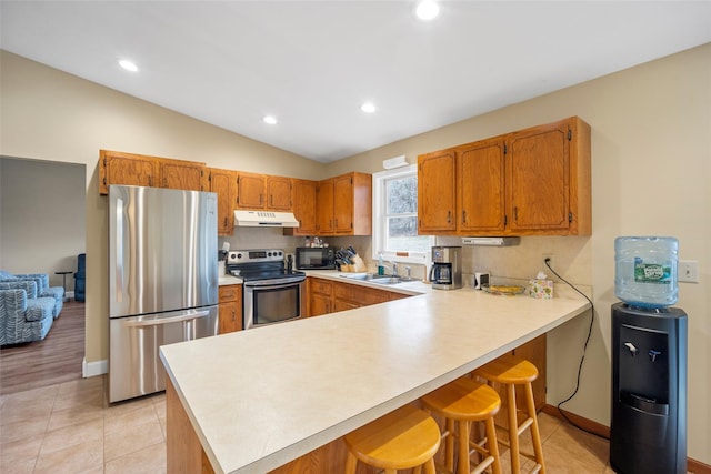 kitchen with under cabinet range hood, light countertops, appliances with stainless steel finishes, a peninsula, and a sink