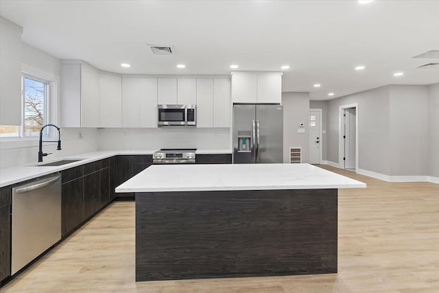 kitchen featuring stainless steel appliances, a kitchen island, light wood-type flooring, and a sink