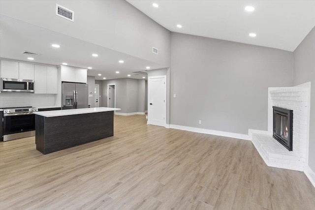 kitchen with visible vents, appliances with stainless steel finishes, light countertops, light wood-type flooring, and a brick fireplace