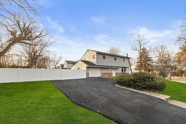 view of front facade featuring brick siding, driveway, a front lawn, and fence