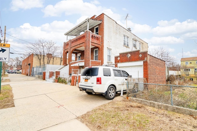 view of side of home featuring a garage, brick siding, concrete driveway, and fence