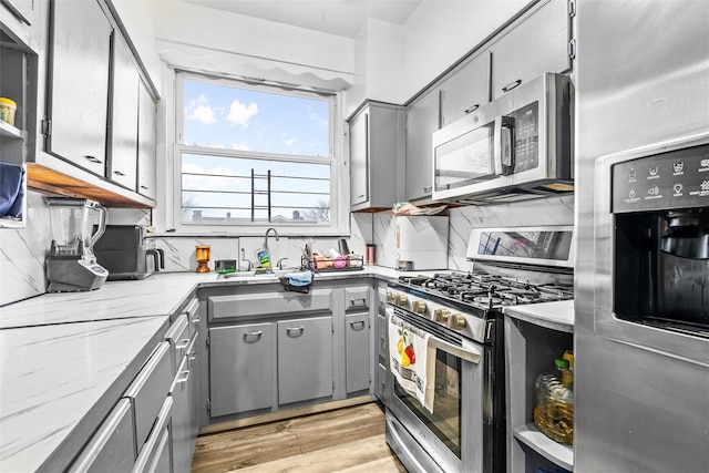 kitchen with decorative backsplash, light wood-style floors, appliances with stainless steel finishes, and gray cabinetry