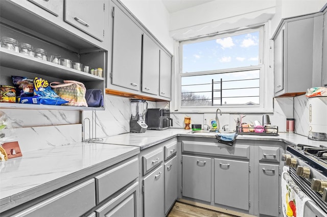 kitchen with stainless steel gas range, open shelves, gray cabinets, a sink, and decorative backsplash