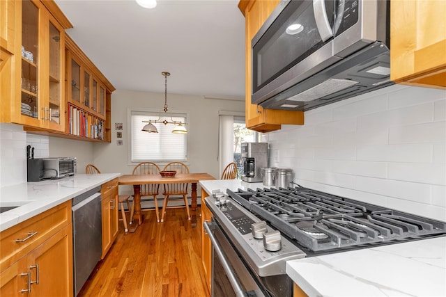 kitchen with light stone counters, brown cabinets, light wood finished floors, appliances with stainless steel finishes, and glass insert cabinets