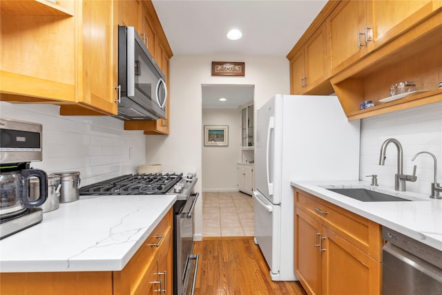 kitchen with open shelves, light wood-style flooring, appliances with stainless steel finishes, brown cabinetry, and a sink