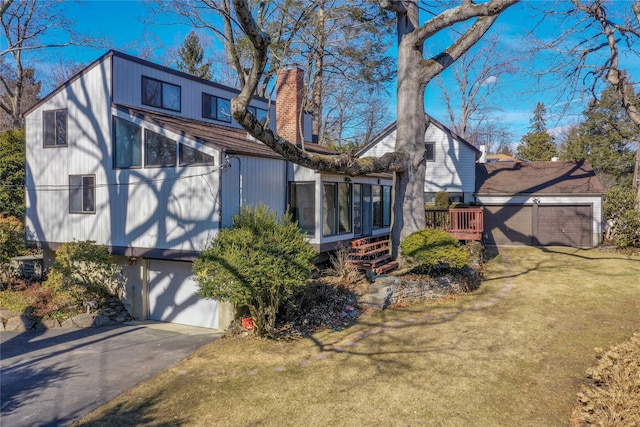 back of house with an attached garage, a yard, driveway, and a chimney