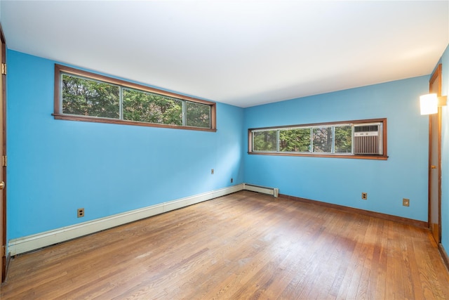 spare room with baseboard heating, a wall unit AC, baseboards, and hardwood / wood-style floors