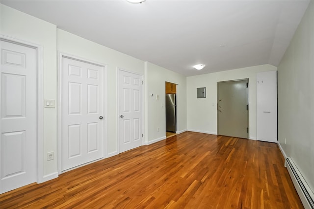 unfurnished bedroom with a baseboard radiator, wood finished floors, multiple closets, electric panel, and freestanding refrigerator