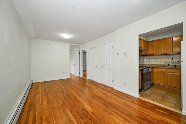 unfurnished living room with a baseboard heating unit, baseboards, a sink, and light wood-style floors