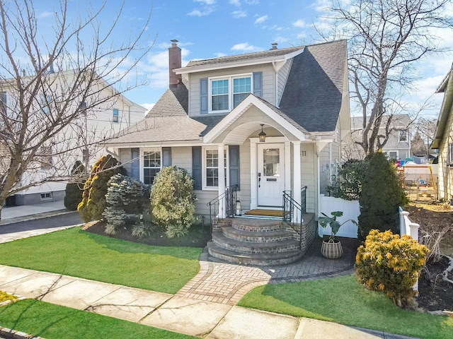 view of front of property featuring a front lawn, roof with shingles, and a chimney