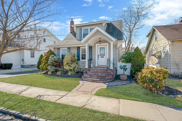 bungalow-style house with a shingled roof, a chimney, and a front yard