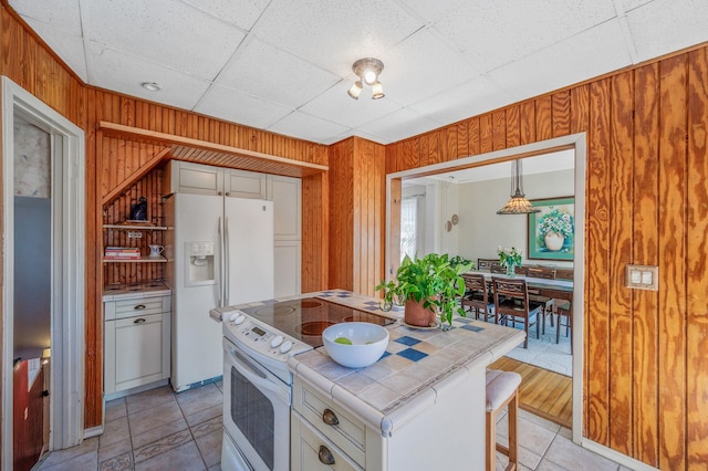 kitchen with white appliances, a drop ceiling, wood walls, and tile countertops