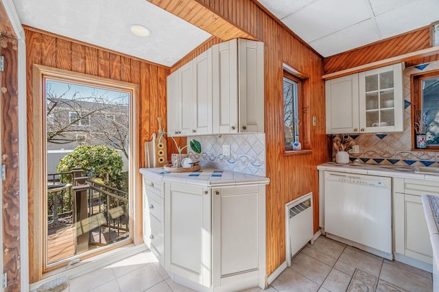 kitchen featuring tile countertops, wood walls, white dishwasher, and backsplash