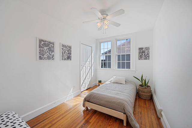 bedroom with a baseboard heating unit, light wood-style flooring, baseboards, and a ceiling fan