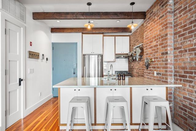 kitchen featuring a breakfast bar, white cabinetry, a sink, stainless steel fridge, and a peninsula