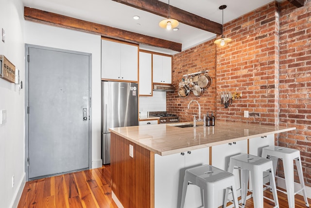 kitchen featuring beam ceiling, freestanding refrigerator, a sink, wood finished floors, and a peninsula