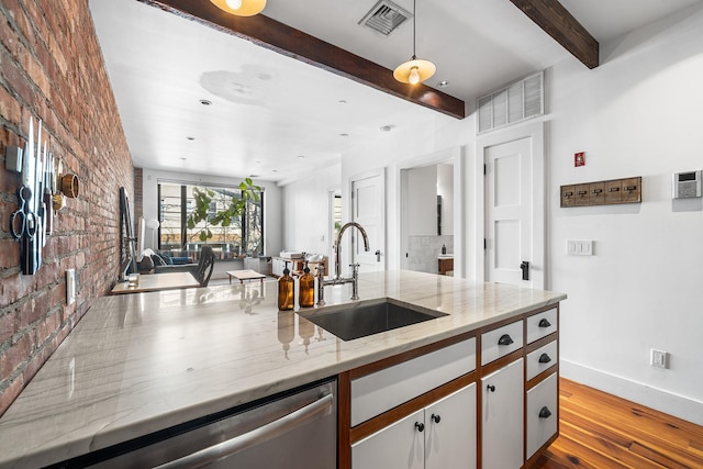 kitchen featuring brick wall, a sink, visible vents, baseboards, and beam ceiling