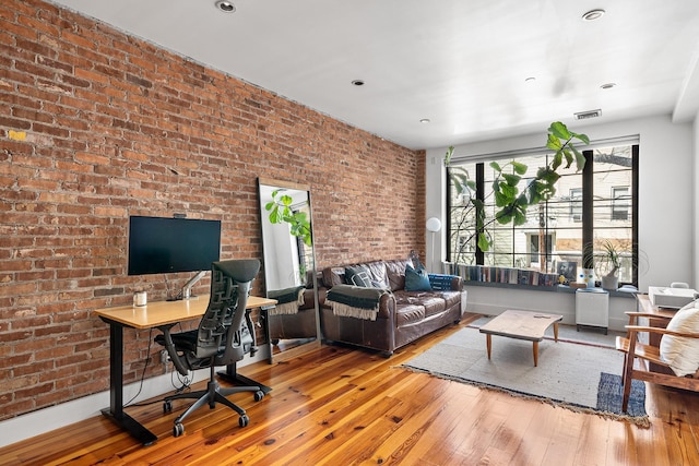 living area featuring brick wall, wood-type flooring, and visible vents