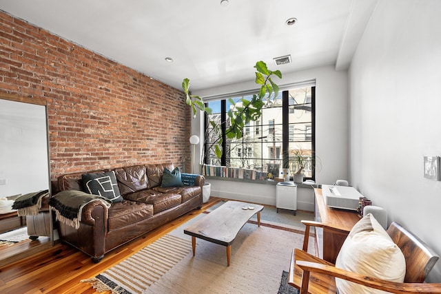 living area featuring brick wall, visible vents, and wood finished floors