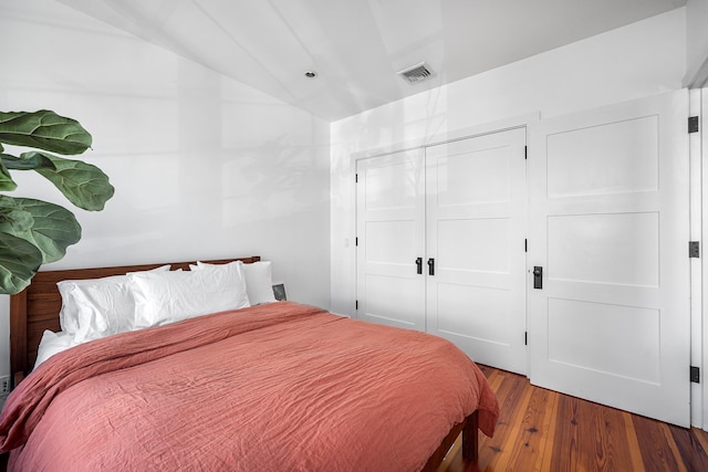 bedroom with a closet, visible vents, vaulted ceiling, and wood finished floors