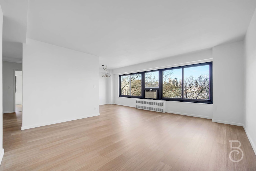 33-65 14th St Unit 5D, Astoria, NY 11106 - unfurnished living room with light wood-style floors, cooling unit, radiator heating unit, a chandelier, and baseboards
