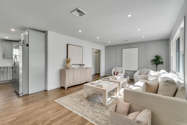 living area with light wood finished floors, visible vents, a decorative wall, and recessed lighting