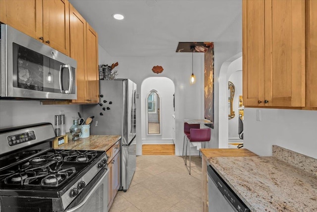 kitchen featuring light tile patterned floors, baseboards, arched walkways, light stone counters, and stainless steel appliances