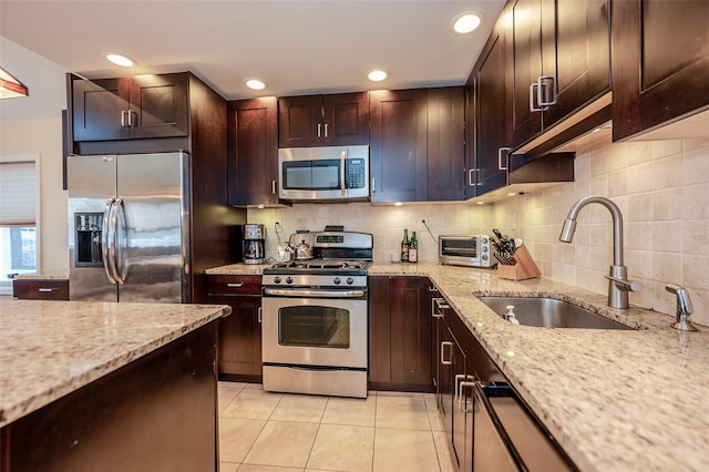 kitchen with light tile patterned floors, light stone counters, a sink, appliances with stainless steel finishes, and decorative backsplash