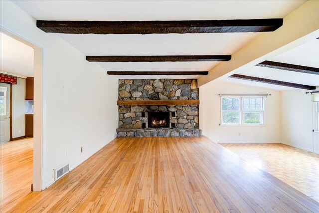 unfurnished living room with baseboards, light wood-type flooring, a stone fireplace, and visible vents