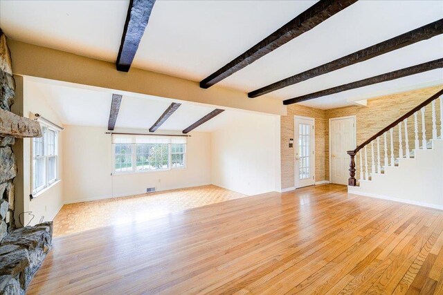 unfurnished living room with visible vents, wood finished floors, baseboards, a stone fireplace, and stairway