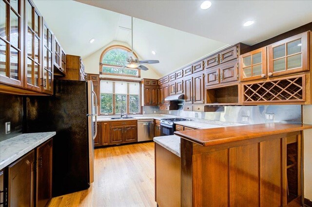 kitchen featuring a sink, stainless steel appliances, a peninsula, lofted ceiling, and light wood-type flooring
