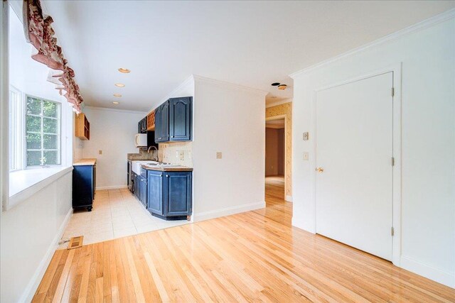 kitchen featuring visible vents, crown molding, light wood-type flooring, light countertops, and blue cabinetry