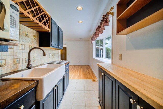kitchen featuring dark cabinetry, wood counters, baseboards, decorative backsplash, and white microwave