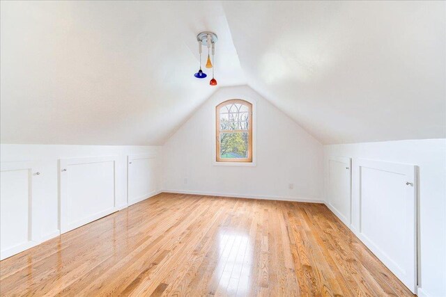 additional living space featuring light wood-style floors, baseboards, and vaulted ceiling