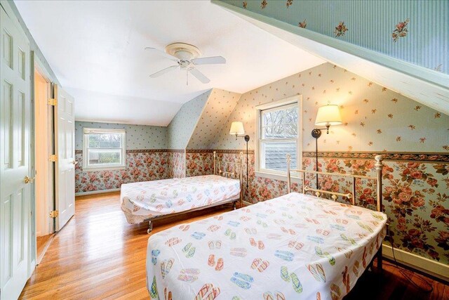 bedroom with wallpapered walls, multiple windows, light wood-style flooring, and a wainscoted wall