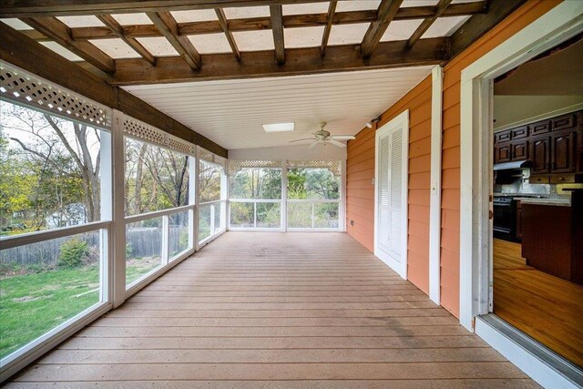 unfurnished sunroom with beam ceiling, wooden walls, hardwood / wood-style floors, and a healthy amount of sunlight